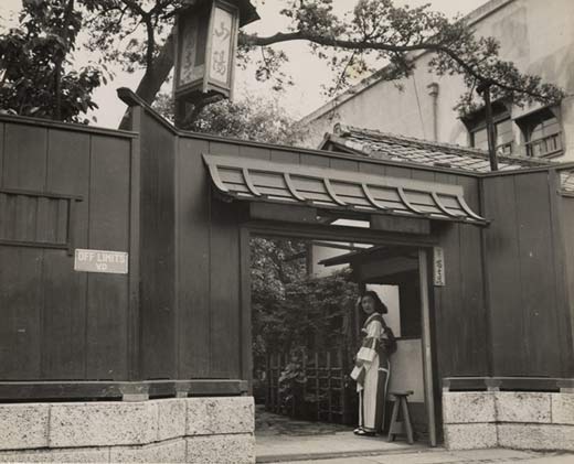 Photographic image of an established house of prostitution. In the doorway is a Japanese woman dressed in traditional clothing and on the wall is a sign written in English that reads 'Off Limits VD'